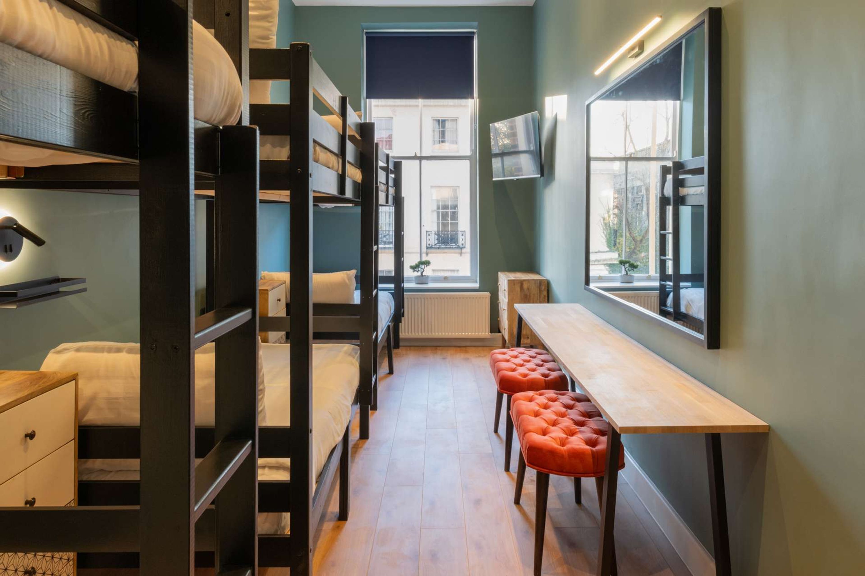 Une chambre de dortoir avec des lits superposés, un bureau en bois et des poufs orange.