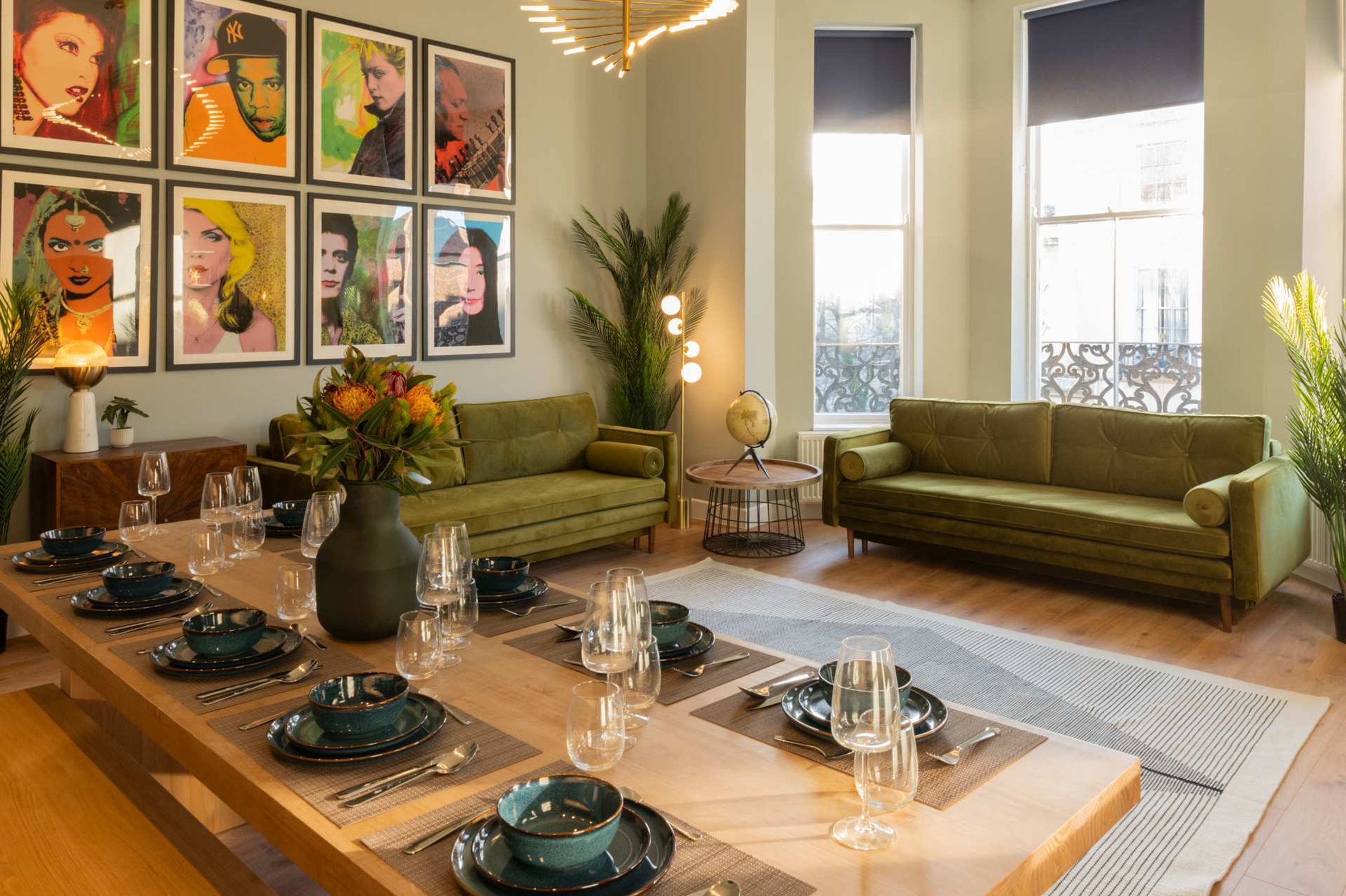 A dining area with a long table set for six, green sofas, and framed artwork on the walls.