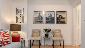 Ein Wohnzimmer mit einer Couch, zwei Sesseln, einem Couchtisch, einer Lampe und drei gerahmten Bildern an der Wand.