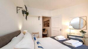 Ein Hotelzimmer mit einem Bett, einem Nachttisch mit Lampe, einem Spiegel und einer Tür zu einem weiteren Raum.