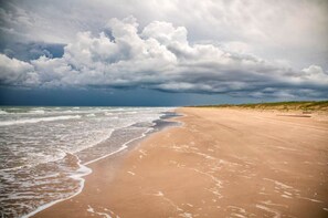 Ein Strand mit breitem Sandstreifen und brechenden Wellen.
