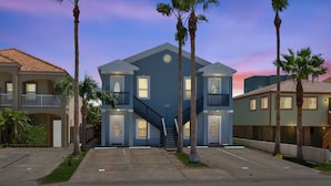 A two-story building with a central staircase, surrounded by palm trees, and a clear sky. - Modern Beachside Condo w Pool - South Padre Island (South Padre Island)