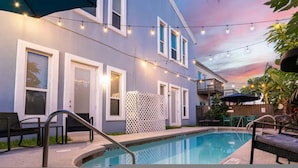 A pool area with a blue house, string lights, and outdoor furniture. - Modern Beachside Condo w Pool - South Padre Island (South Padre Island)