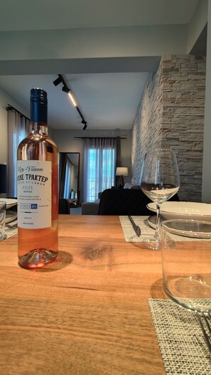 A bottle of wine on a wooden table with a glass and a plate, in a room with a stone wall and a bed in the background. - Alaia Haven Elegant Holiday Home in Kefalonia (Kefalonia)