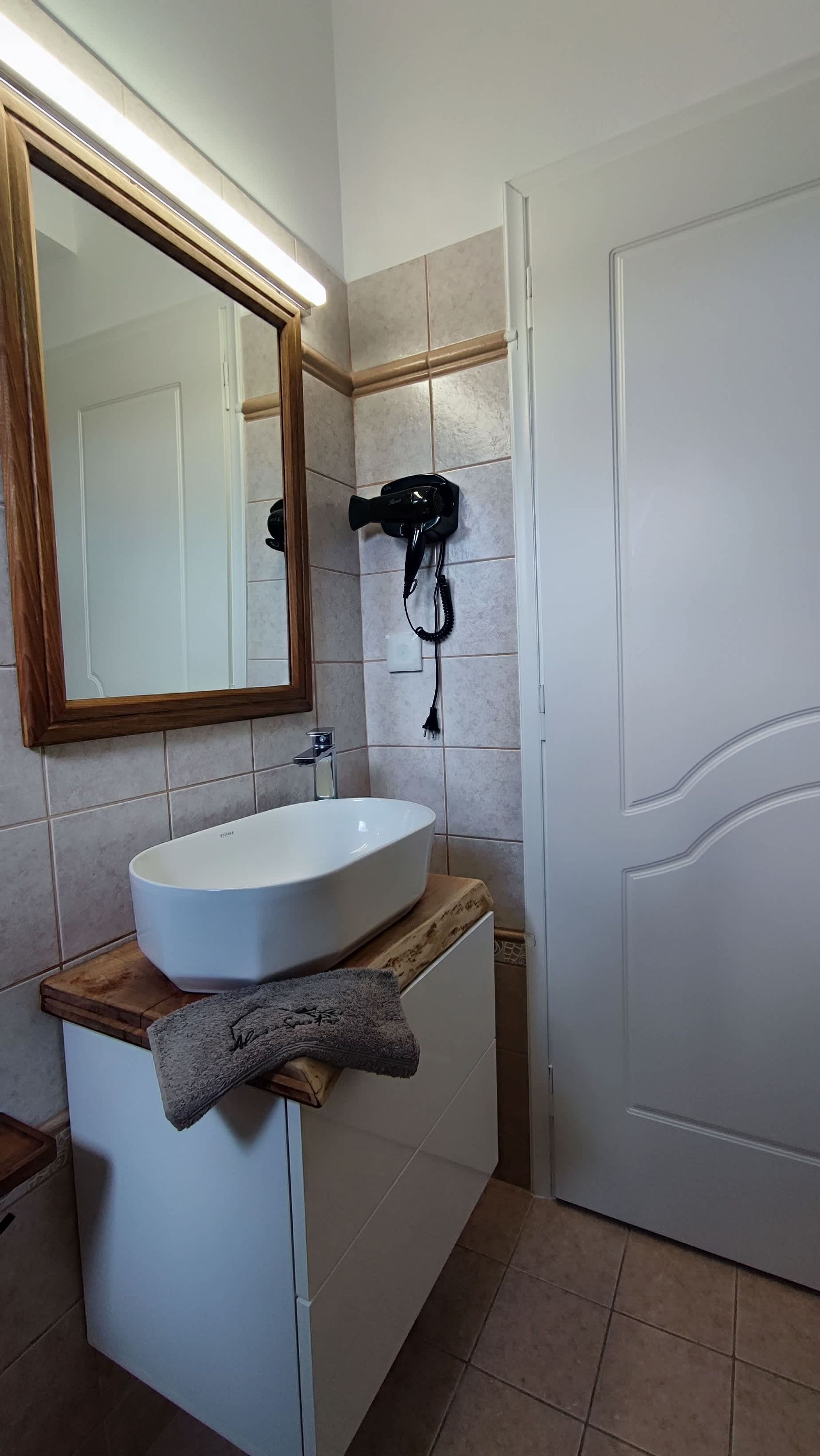 A bathroom with a white sink, a wooden countertop, a mirror with a wooden frame, and a hairdryer on the wall.
