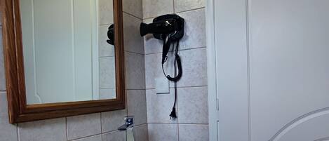 A bathroom with a white sink, a wooden countertop, a mirror with a wooden frame, and a hairdryer on the wall.