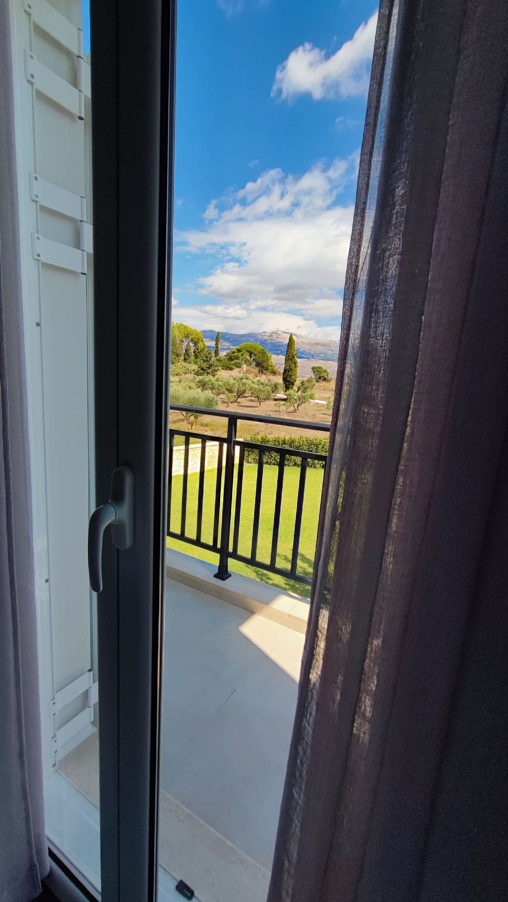 A balcony with a view of a landscaped garden and distant mountains.