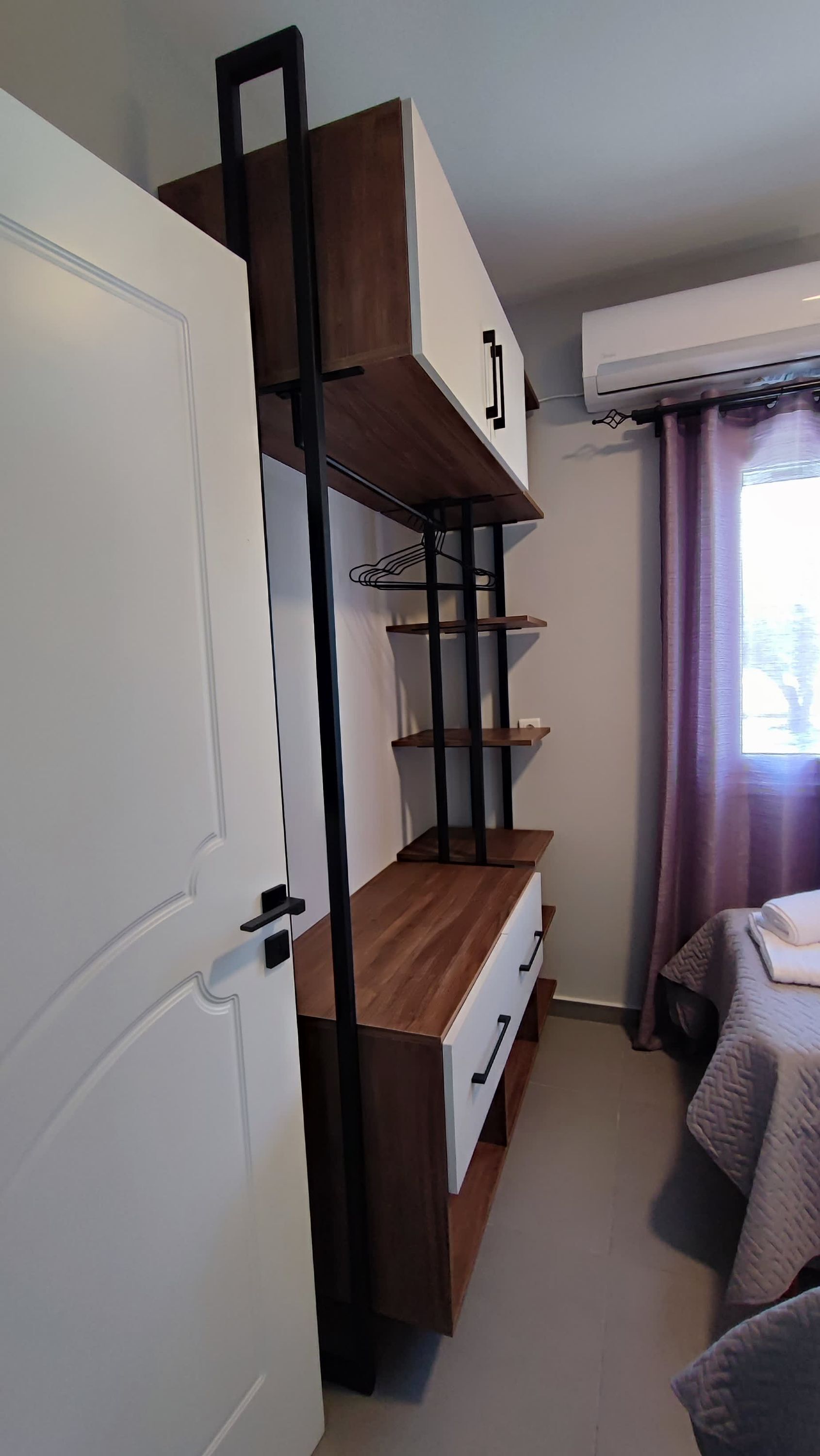 A compact bedroom with a bunk bed, a white wardrobe, a small desk, and a bed with a patterned bedspread.