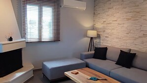 A modern living room with a stone wall, a grey sofa, a wooden coffee table, and a fireplace. - Alaia Kefalonia Garden Haven Elegant Holiday Home (Kefalonia)