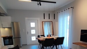 A modern living room with a sofa, a wooden coffee table, and a dining area with a table and chairs. There is a kitchen area with a refrigerator and oven. - Alaia Kefalonia Garden Haven Elegant Holiday Home (Kefalonia)