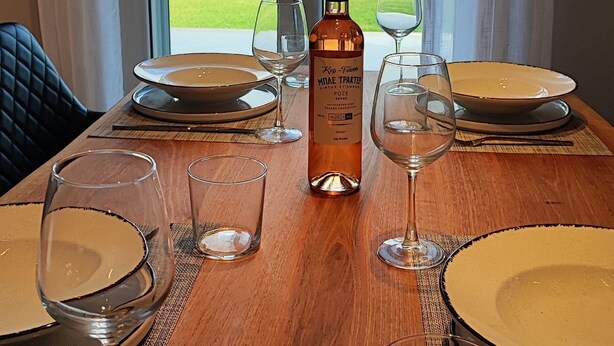 A dining table with plates, glasses, and a bottle of wine, set against a backdrop of a scenic outdoor view through large windows. - Alaia Kefalonia Garden Haven Elegant Holiday Home (Kefalonia)