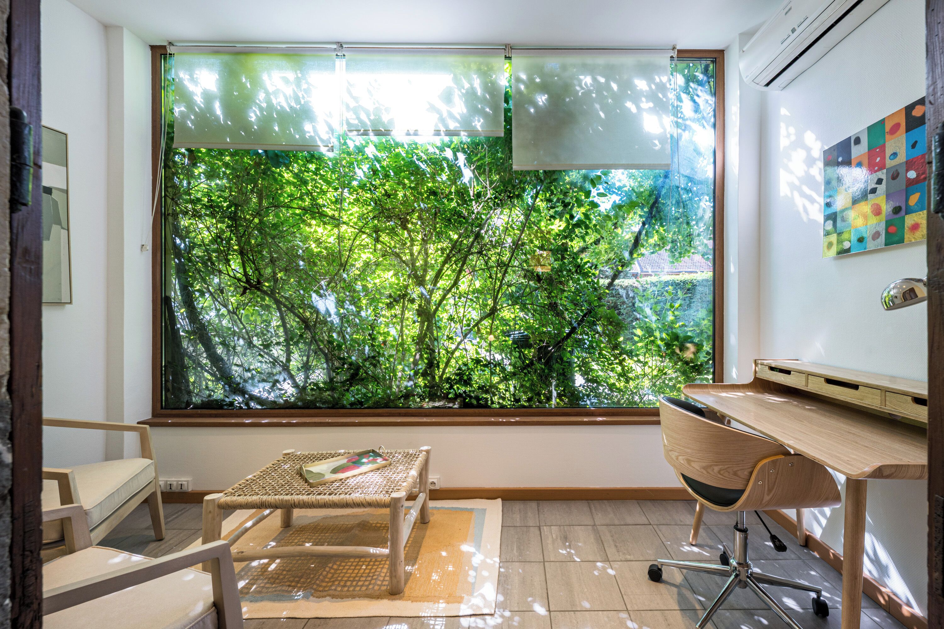 A room with a large window, a desk, a chair, and a small table.