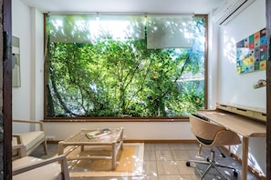 Ein Zimmer mit einem großen Fenster, einem Schreibtisch, einem Sessel und einem kleinen Tisch.