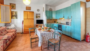 Un soggiorno con divano, tavolo da pranzo, sedie e angolo cottura con pensili color acquamarina e microonde.