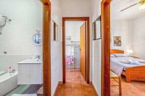 Um corredor estreito que leva a um quarto com cama de madeira, um banheiro com banheira e um armário com prateleiras.