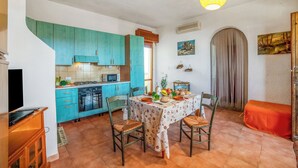 A kitchen with teal cabinets, a dining table with chairs, and a hanging light fixture. - Favoloso Salento - Flat With Balcony 50m to Beach (Maruggio)