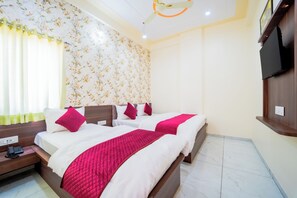 Habitación de hotel con dos camas, cabecero de madera, ventilador de techo, televisor montado en la pared y diseño de papel tapiz floral.