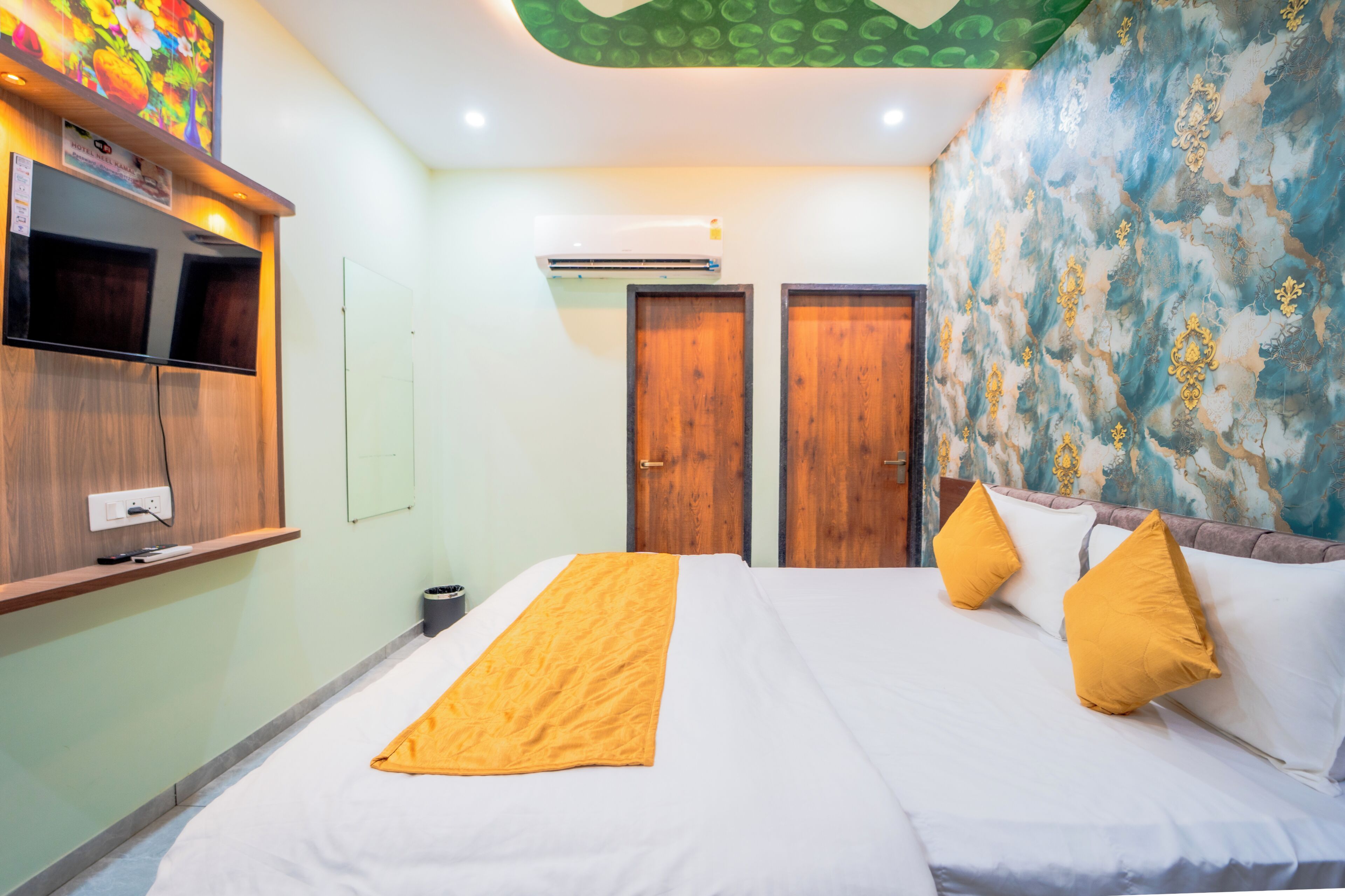 A hotel room with a bed, a television, an air conditioning unit, and a wall with a decorative pattern.