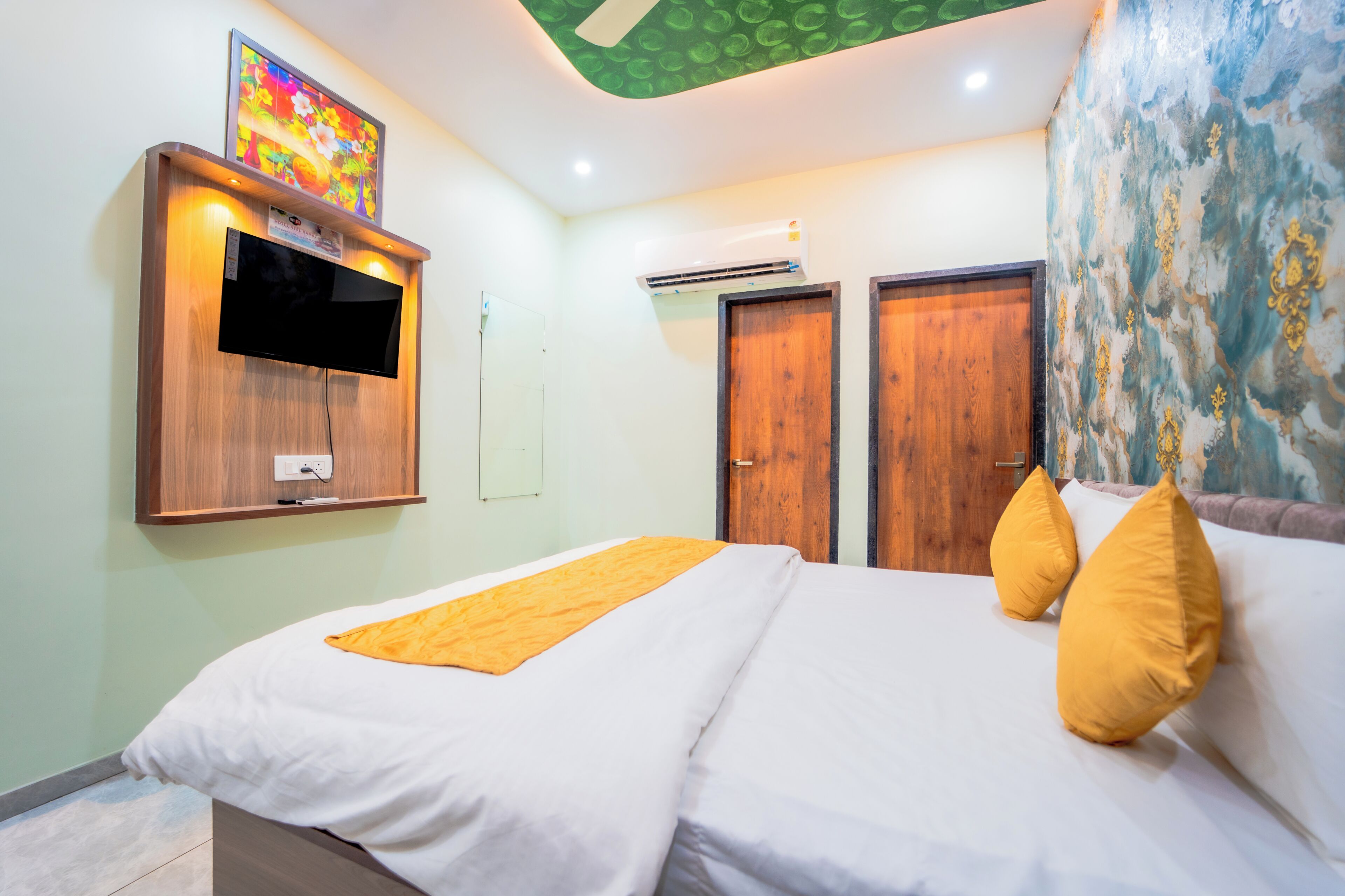 Een slaapkamer met een bed, een aan de muur bevestigde televisie, een airconditioning en twee houten deuren.