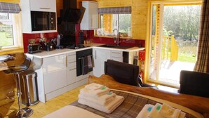 A compact kitchen with white cabinets, a microwave, and a sink. There is a window with a view of greenery outside. - The Balmoral Studio Lodge – Private Hot Tub & On-Site Carp Fishing 🎣🛁 (Ellesmere)