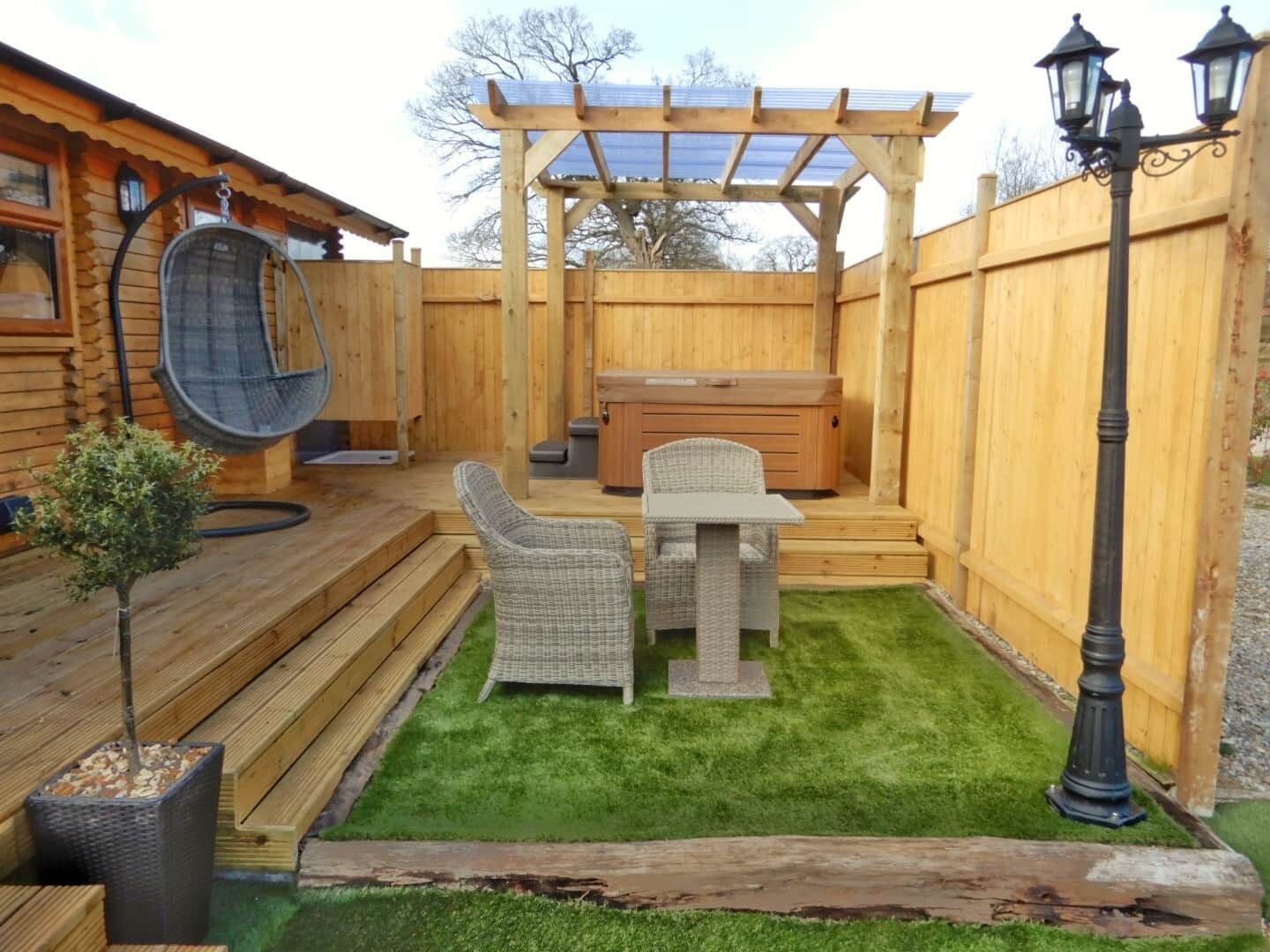 Eine Holzterrasse mit Whirlpool, Korbstühlen und einer Pergola.