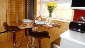 A wooden interior with a dining table set for two, a window with a view, and a microwave on a white countertop. - The Balmoral Studio Lodge – Private Hot Tub & On-Site Carp Fishing 🎣🛁 (Ellesmere)