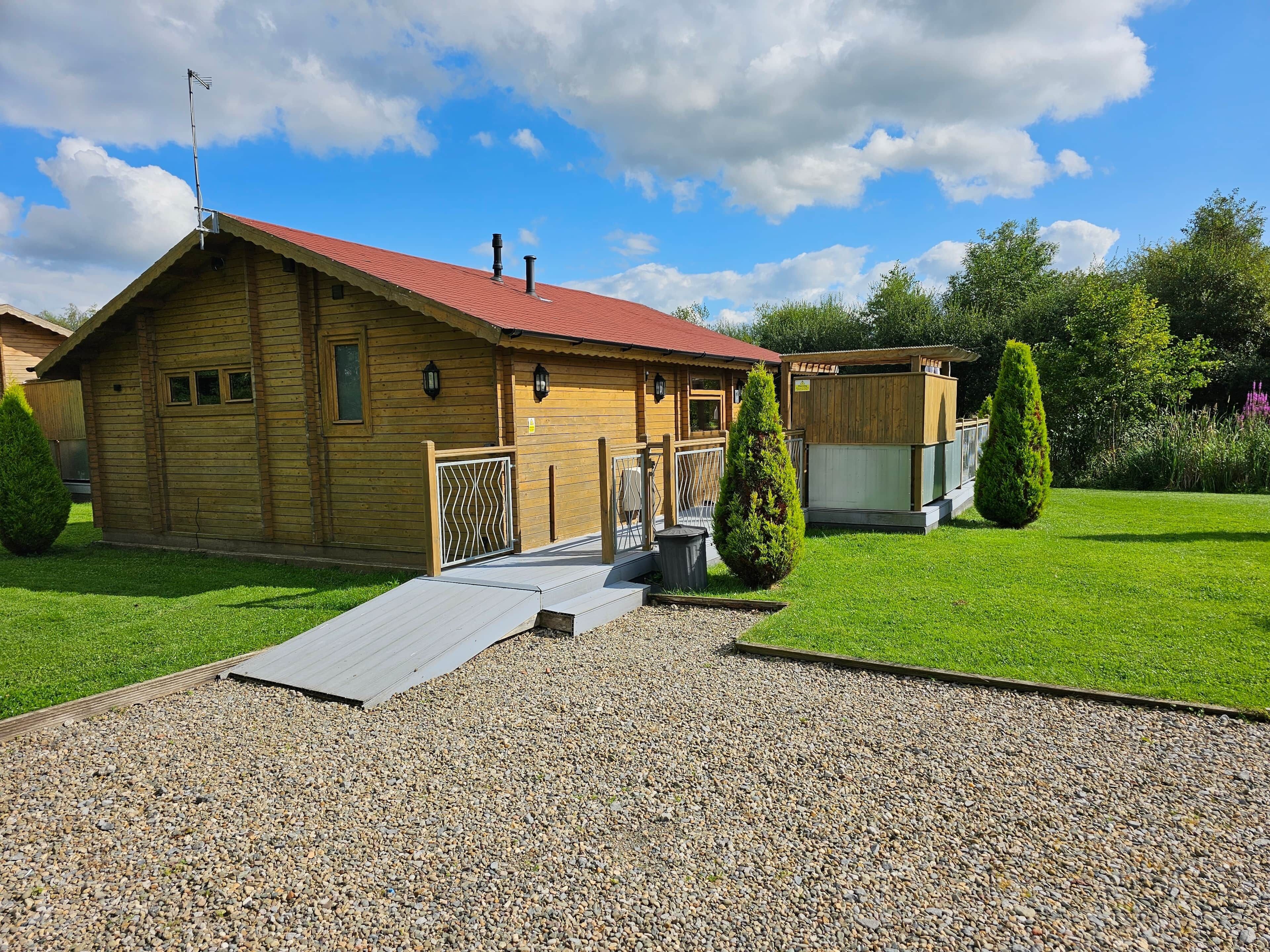 A wooden cabin with a red roof, a gravel driveway, and a fenced garden area.