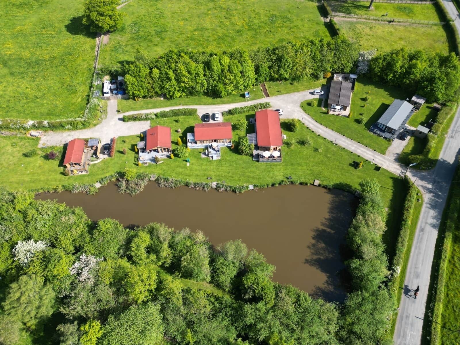 An aerial view of a rural property with multiple red-roofed buildings, a pond, and surrounding greenery.