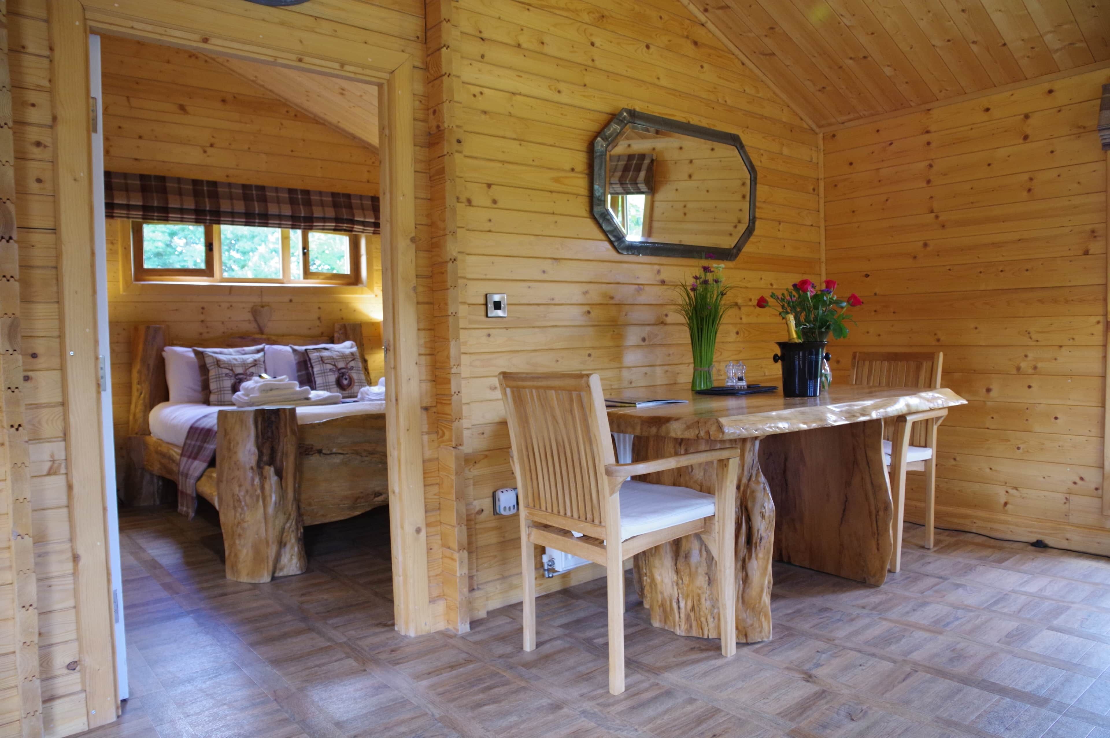 Een gezellig houten cabin interieur met een eettafel, stoelen, een bank en een spiegel aan de muur.