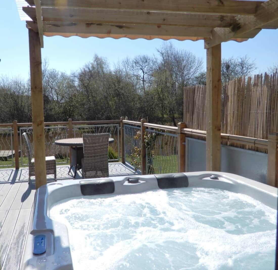 Un jacuzzi bajo una pérgola de madera, con una mesa y sillas cerca.