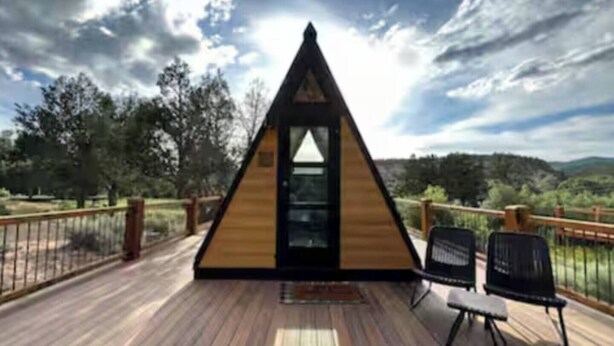 A triangular wooden structure with a door, a deck, and two chairs.