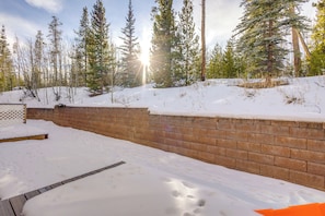 A snow-covered outdoor area with a brick wall and wooden steps leading up to a wooden deck. - Heated Pool Access at Winter Park Base Camp! (Winter Park)