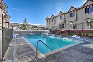 A swimming pool with a metal ladder, surrounded by a stone deck, and adjacent to a building with a balcony. - Heated Pool Access at Winter Park Base Camp! (Winter Park)