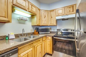 A kitchen with wooden cabinets, a stainless steel refrigerator, a microwave, a stove, and a dishwasher. - Heated Pool Access at Winter Park Base Camp! (Winter Park)
