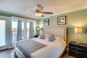 A bedroom with a large bed, a ceiling fan, a nightstand with a lamp, and a view of the outdoors through the window. - Walk to Beach! Pet-friendly Mustang Island Retreat (Port Aransas)
