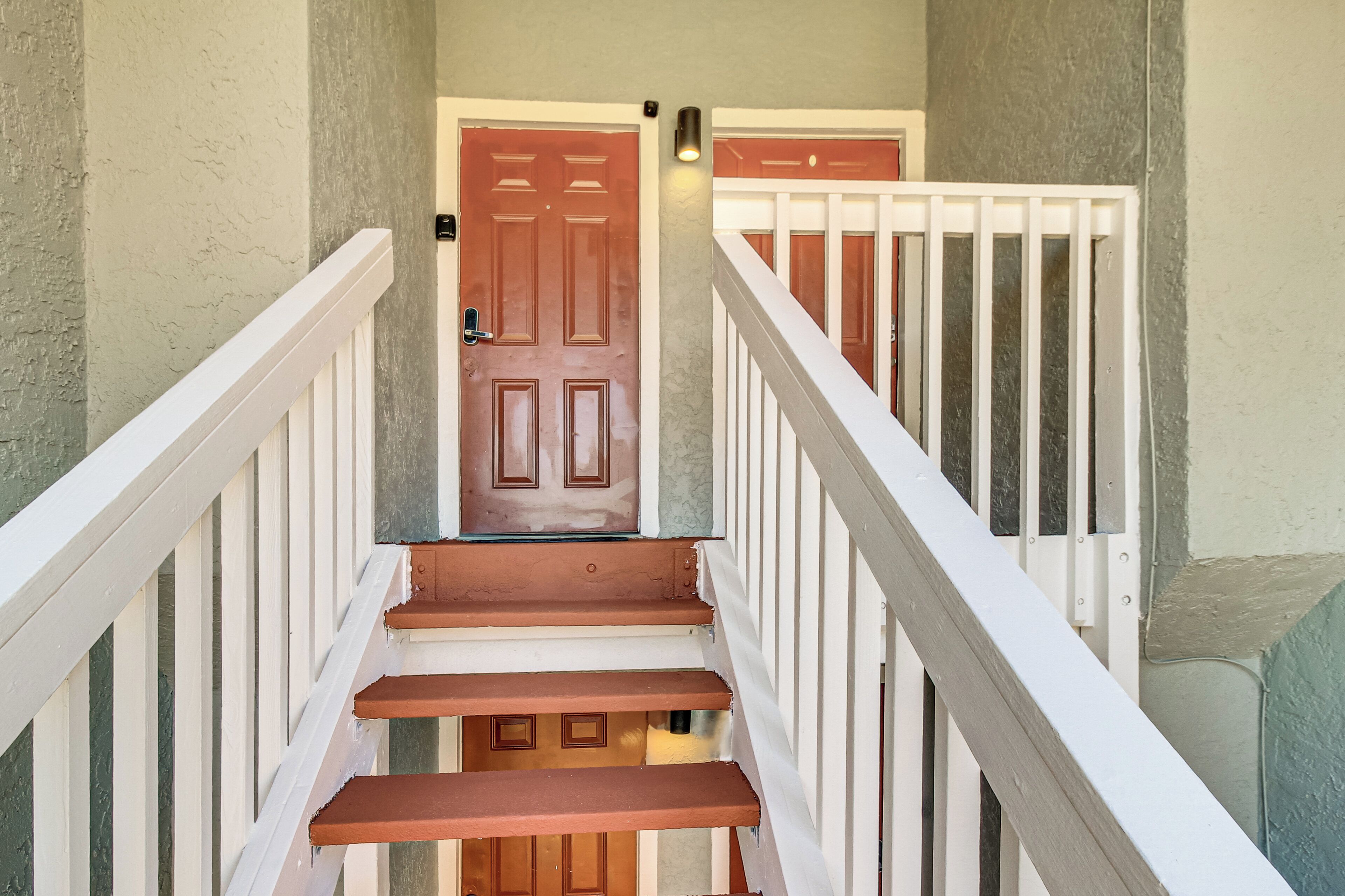 A staircase with white railings and wooden steps leading to a door with a light fixture above it.