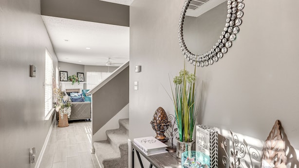 Un interior moderno con una escalera que lleva a una sala de estar, un espejo decorativo y una mesa con diversos objetos.