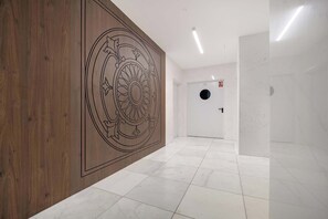 Ein Korridor mit einer Holzverkleidung und dekorativem Muster, weiß gefliestem Boden und einer Tür mit rundem Fenster.