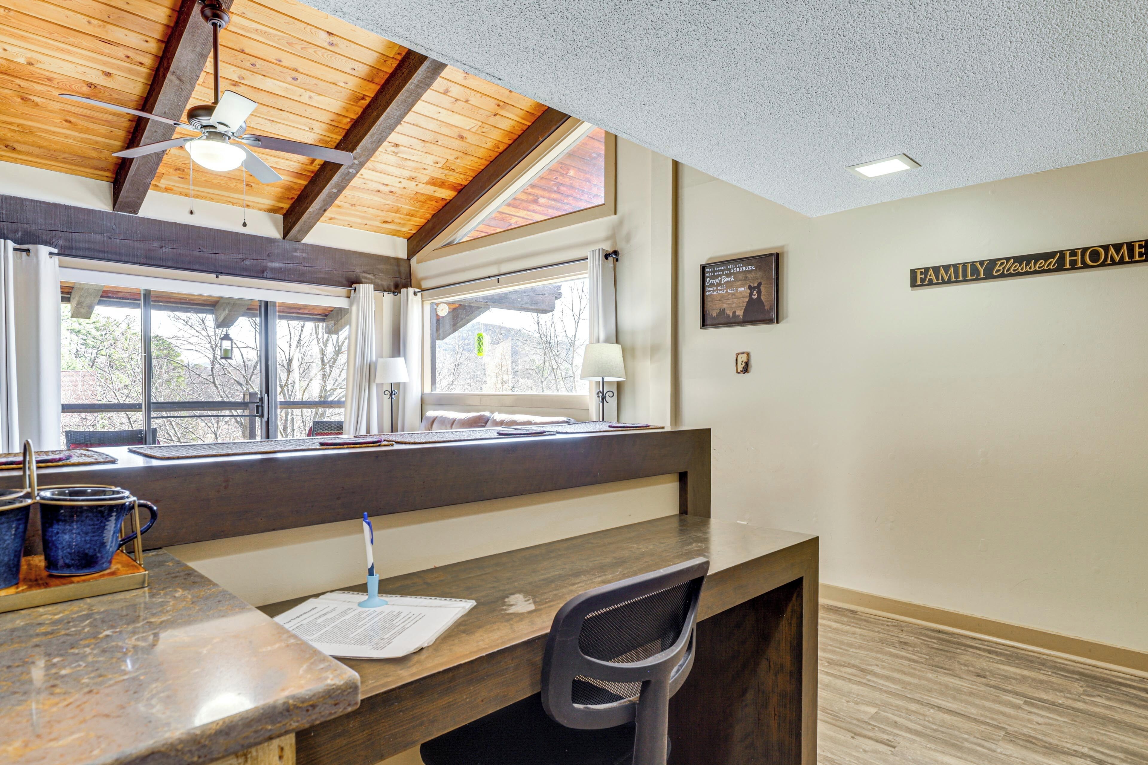 A kitchen area with a wooden ceiling, a window with curtains, a countertop with a chair, and a sign on the wall.