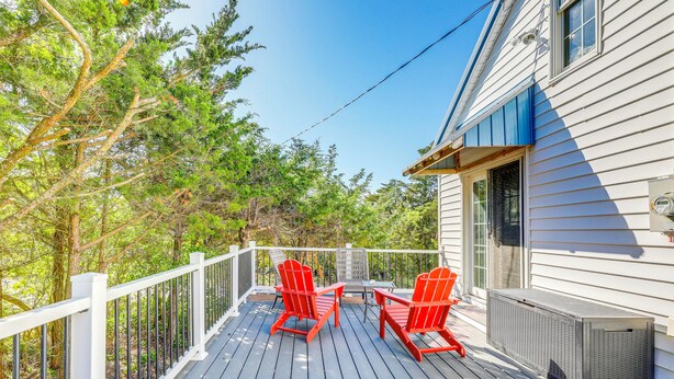 A wooden deck with two red Adirondack chairs and a table, a white railing, and a house with siding and a window. - Walk to Broadkill Beach: Sleek Family Home w/ Deck (Milton)