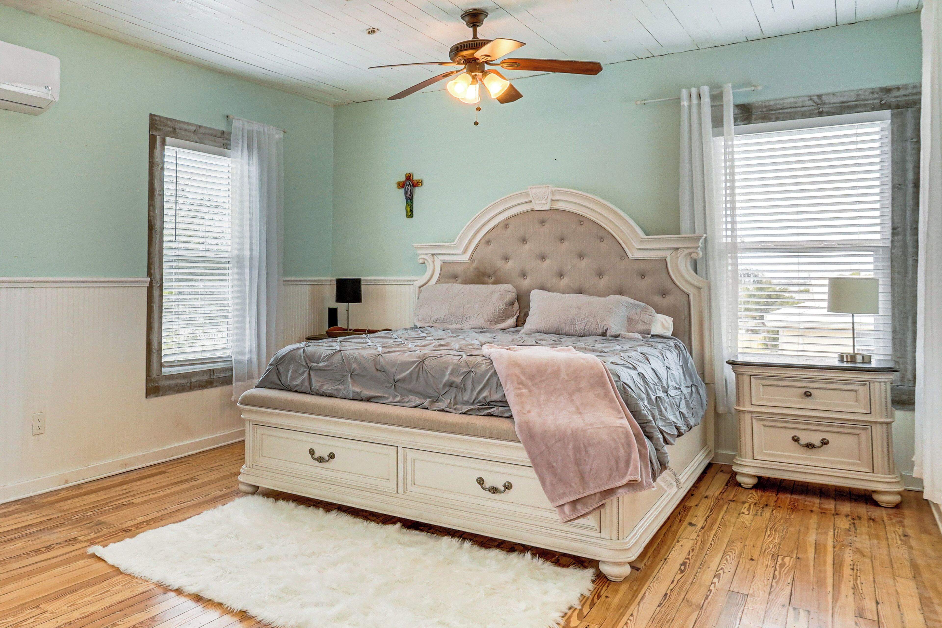 A bedroom with a large bed, a nightstand, a ceiling fan, and a window with blinds.