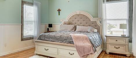 A bedroom with a large bed, a nightstand, a ceiling fan, and a window with blinds.
