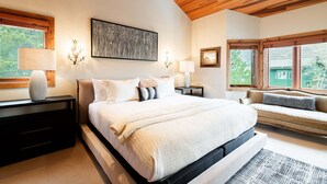 Ein Schlafzimmer mit einem großen Bett, Nachttischen, einer Bank und Blick auf Grünflächen.