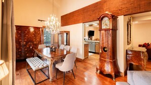 Ein Essbereich mit Holztisch, gepolsterten Stühlen, einer Bank, einer Chandelier und einer Standuhr.