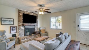 Una sala de estar con chimenea de ladrillo, ventilador de techo, televisor de pantalla plana y sofá gris.