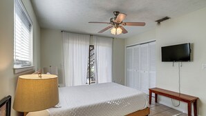 Un dormitorio con cama, ventilador de techo, televisor y ventana con cortinas.
