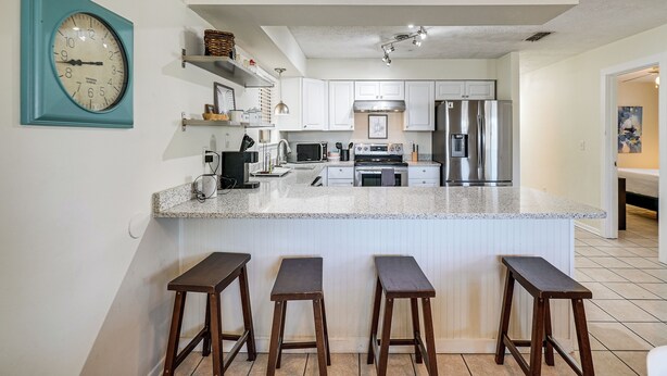 Una cocina moderna con armarios blancos, un refrigerador de acero inoxidable, un microondas y una isla grande con taburetes de bar.