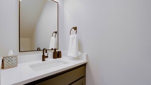 Un baño con un lavamanos blanco, un espejo grande y un perchero para toallas.