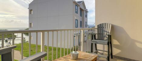 A balcony with a wooden table and a metal bucket, overlooking a grassy area and a body of water.