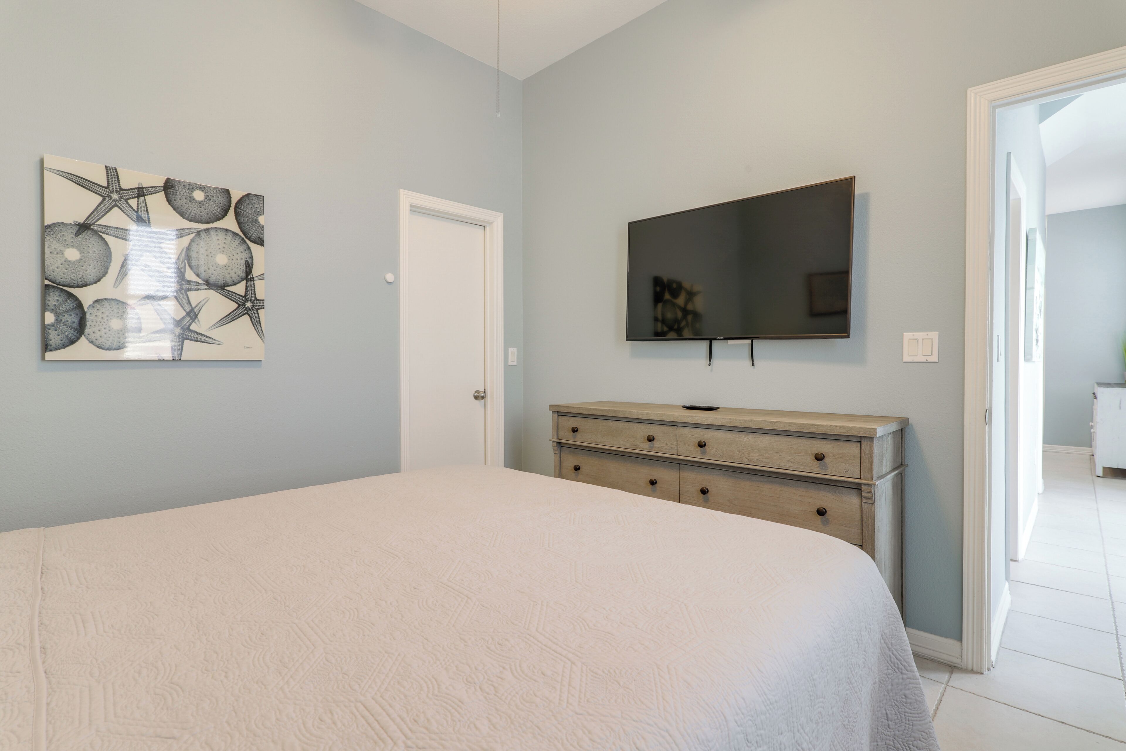 A bedroom with a bed, a dresser, a TV, and a wall art piece.